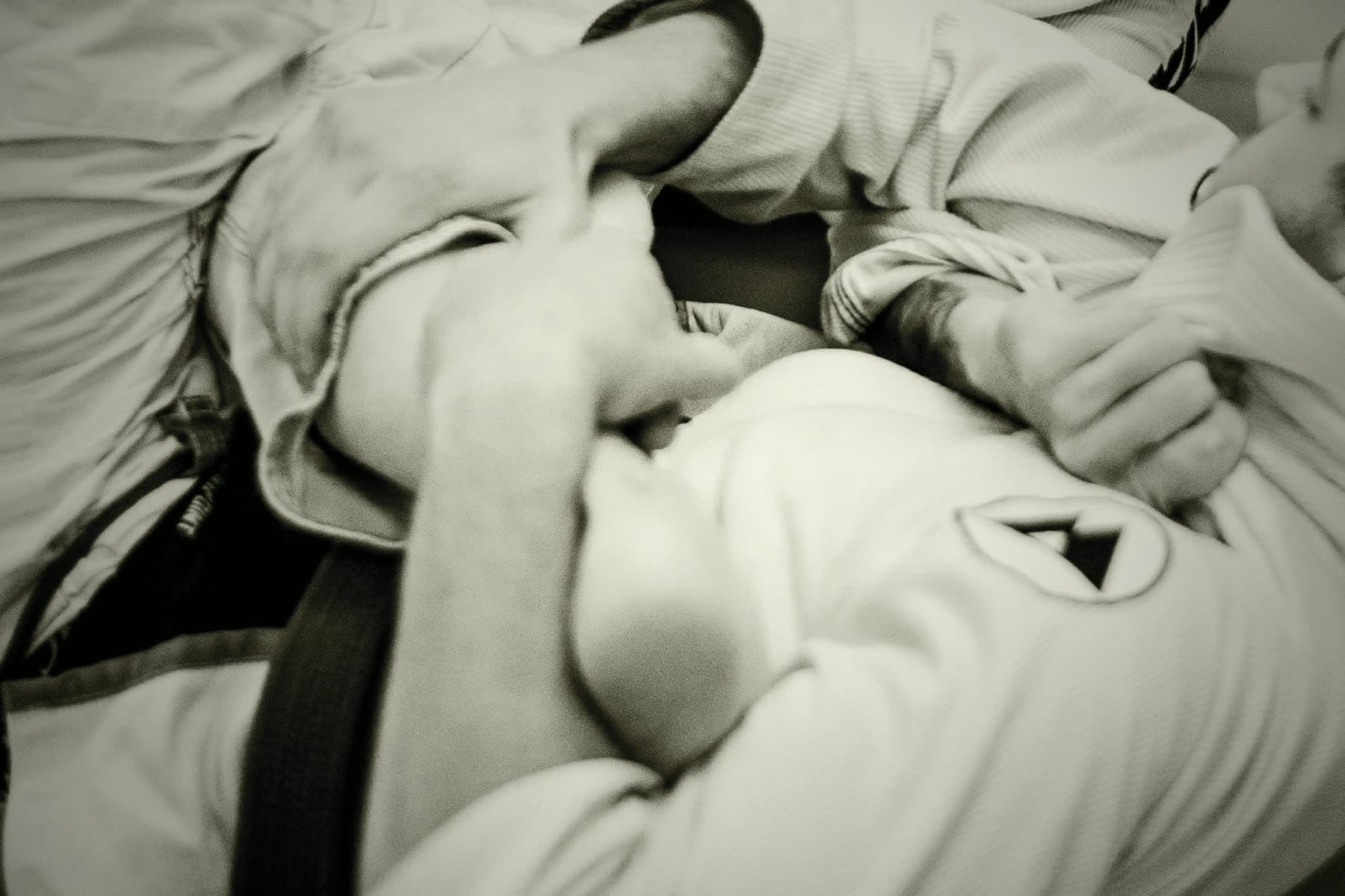 Hands gripping a gi mid-roll on the mats, belt in frame