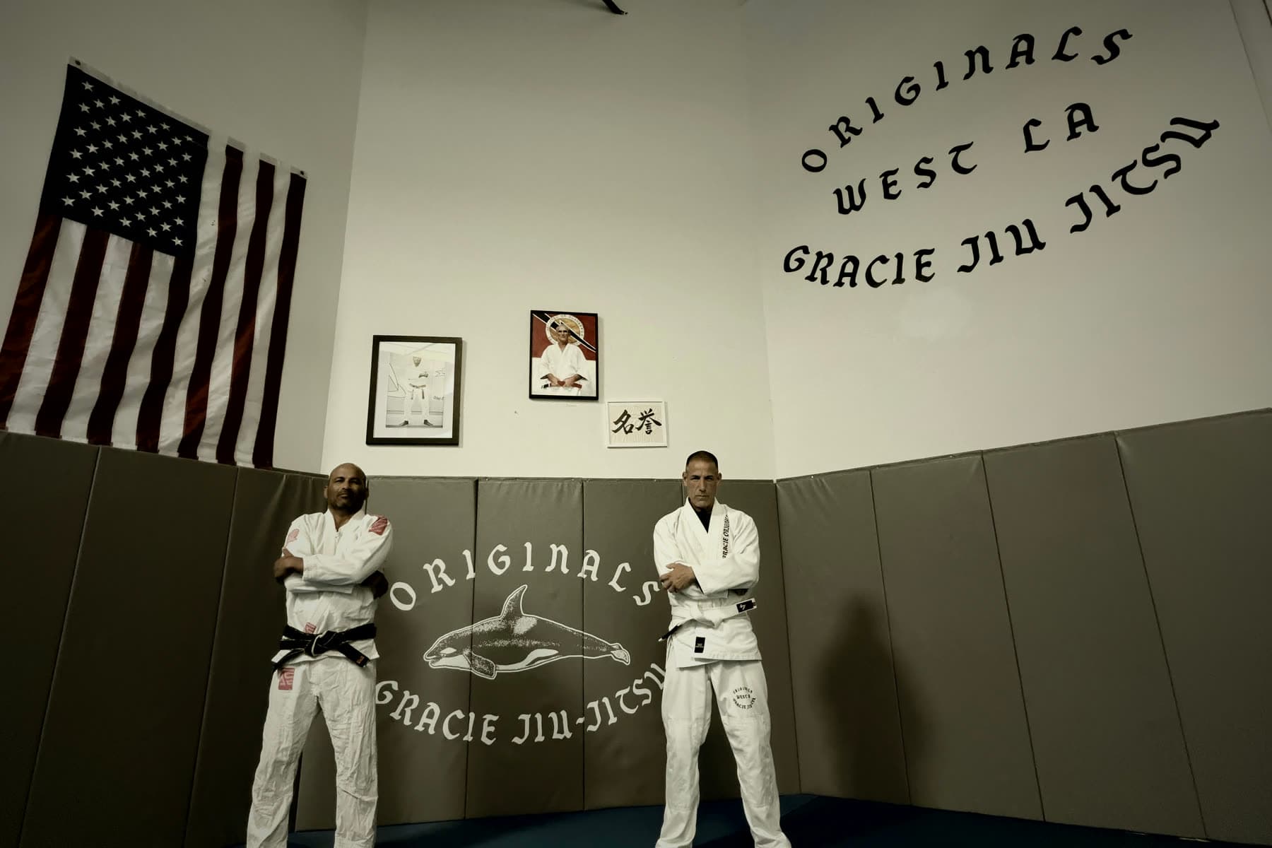 Two practitioners in gis standing on the mats beneath the lineage wall at Gracie Originals in Santa Monica