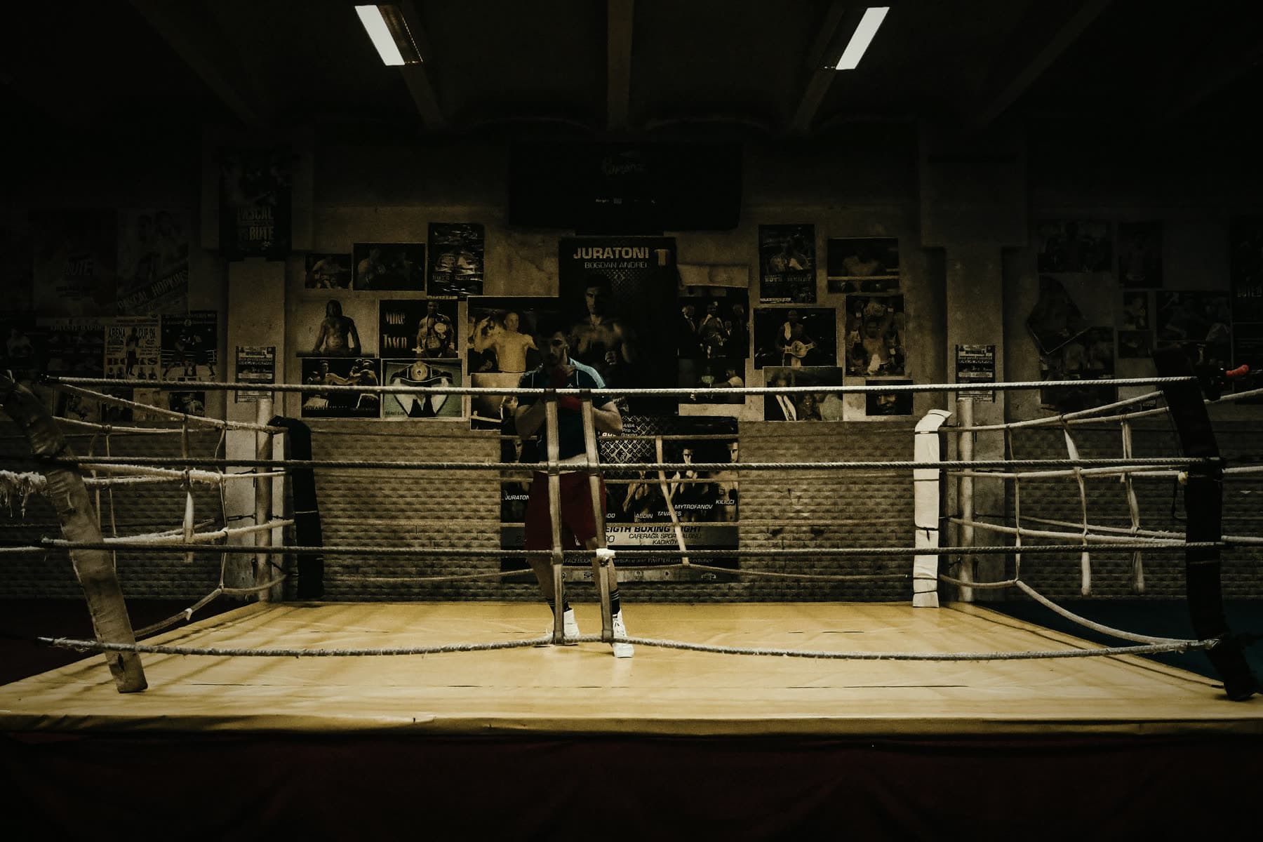 An old boxing ring under warm light, a lone figure training in the distance