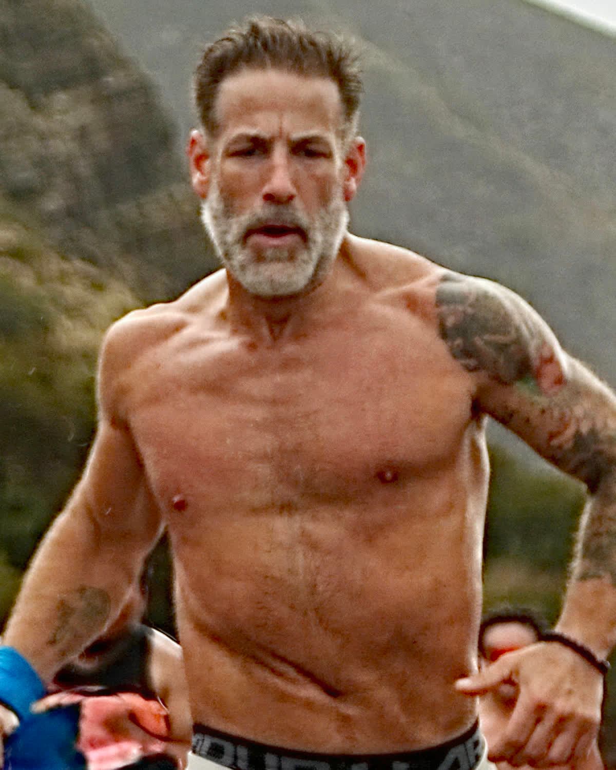 Marc Weintraub mid-stride near the finish of a road race, coastal hills behind him