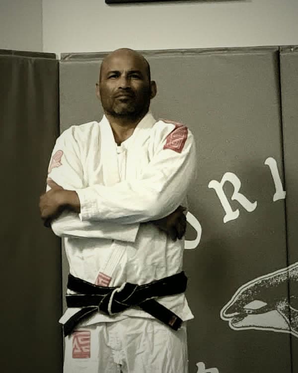 Richard Salgado in his gi, arms crossed, black belt visible, on the mats